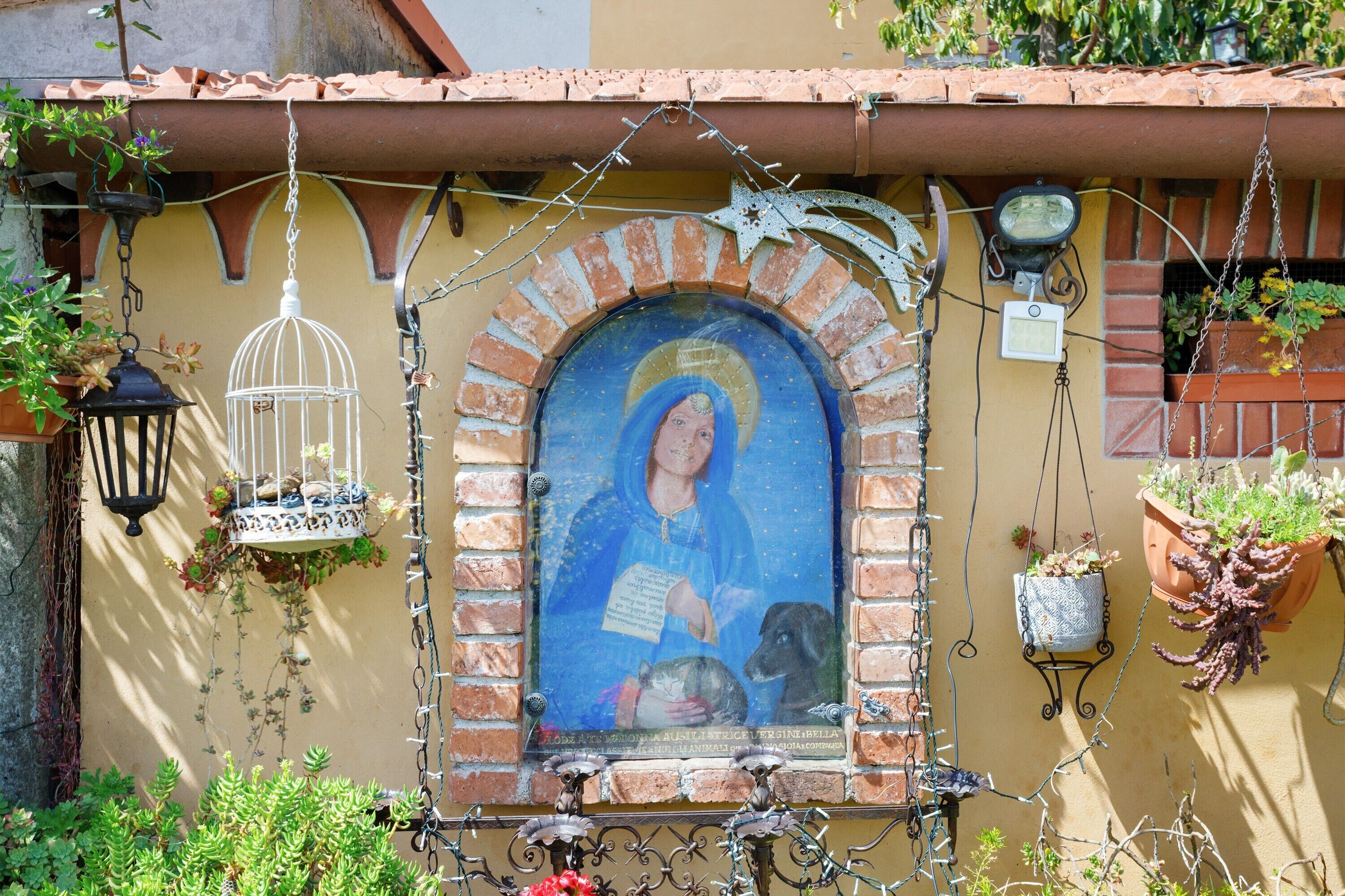 Un murale raffigura una figura religiosa, un arco in mattoni, vasi pensili e un piccolo cane.
