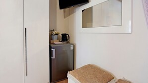 Een compacte kamer met een kitchenette, een flatscreen televisie aan de muur en een zithoekje met een gestreept kussen.