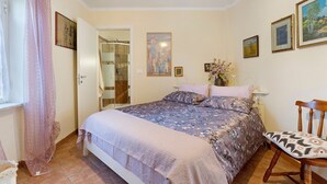Een slaapkamer met een bed, een stoel, een raam met gordijnen en een kunstwerk aan de muur.