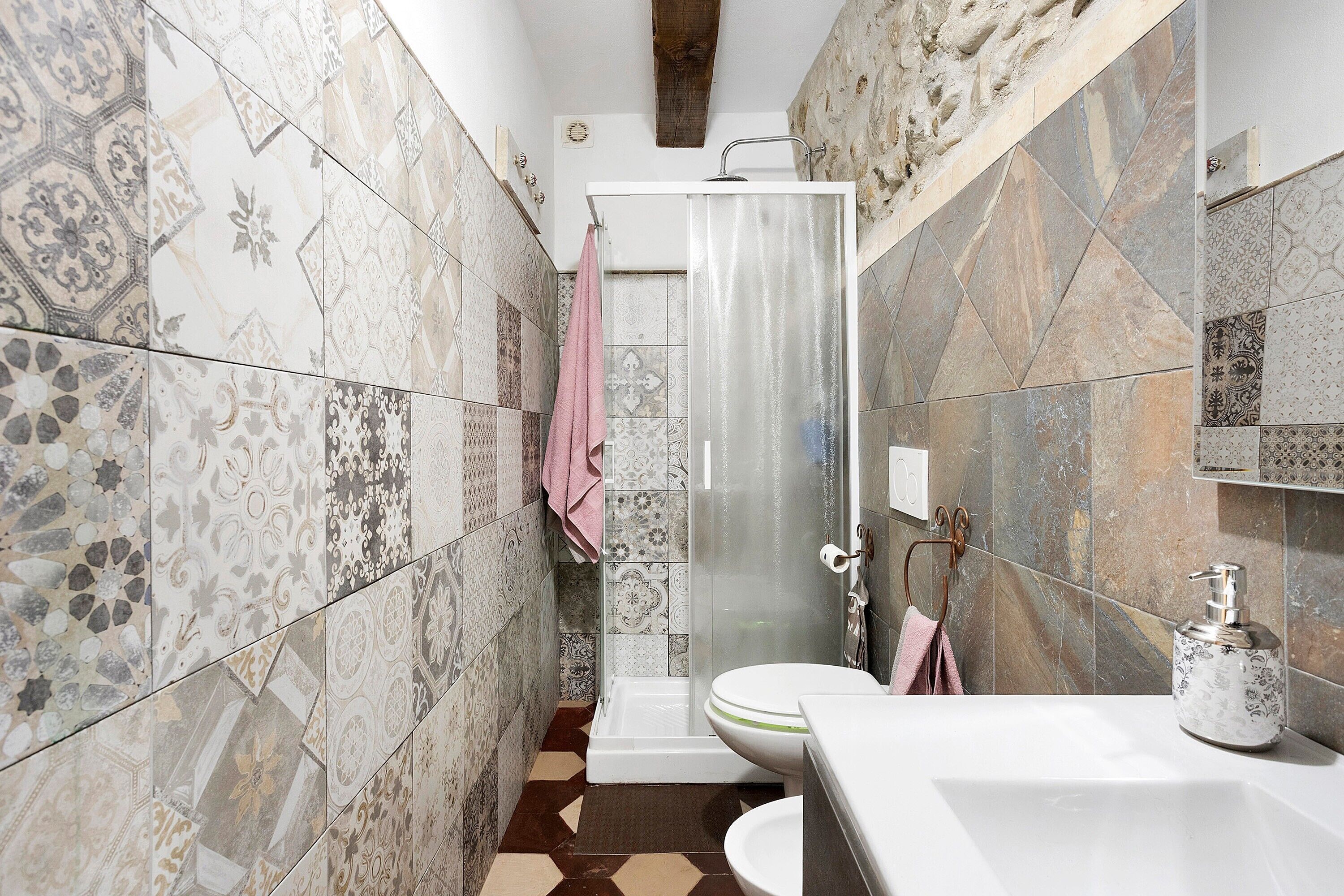 A bathroom with patterned tiles, a shower, a toilet, and a sink with a soap dispenser.