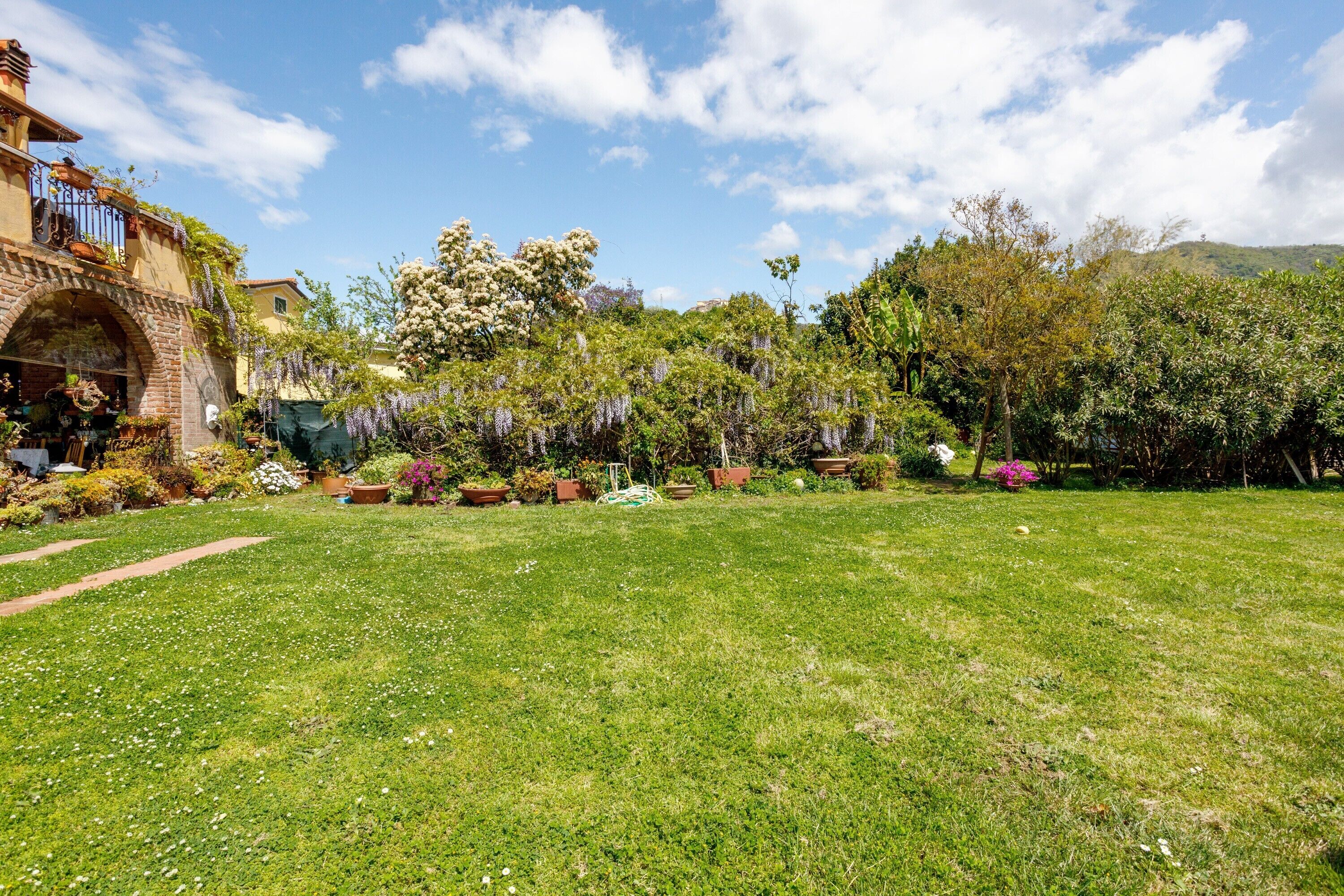 A garden with a brick archway, potted plants, and a variety of trees.