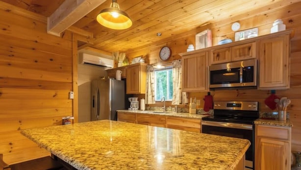 Una cocina con gabinetes de madera, encimera de granito, electrodomésticos de acero inoxidable y una lámpara colgante.