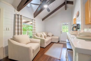 A cozy room with a sofa, a chair, a kitchen area, and a view through a window. - 5BDR Modern Farm Compound: Pool, Hot Tubs, Trails (Sevierville)
