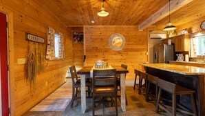 Un interior de madera con una mesa de comedor, sillas, una zona de cocina y un reloj en la pared.