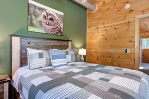 Ein Schlafzimmer mit einem Holzkopfstück, einer gesteppten Bettdecke und einem gerahmten Bild von einer Eule an der Wand.