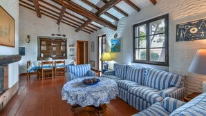 A rustic interior with exposed wooden beams, a stone wall, a dining area with striped blue and white furniture, and a large window. - Villa La Colombaia on Elba Island (Campo nell'Elba)