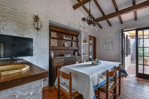 Une pièce rustique avec une table en bois, des chaises, un téléviseur et un mur en briques blanches.