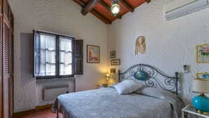 A bedroom with a bed, a window with shutters, a wall-mounted air conditioner, and a decorative lamp. - Villa La Colombaia on Elba Island (Campo nell'Elba)