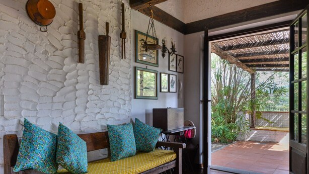A room with a stone wall, wooden bench with cushions, framed pictures, and a view of greenery outside. - Villa La Colombaia on Elba Island (Campo nell'Elba)