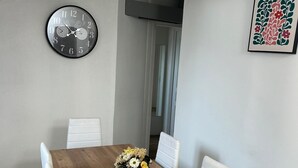 En matplats med ett träbord, vita stolar, en klocka och ett blommotiv på väggen.