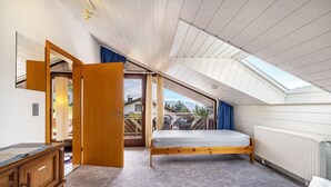 Une chambre avec un plafond en pente, un lit en bois, une commode et une vue sur l’extérieur.