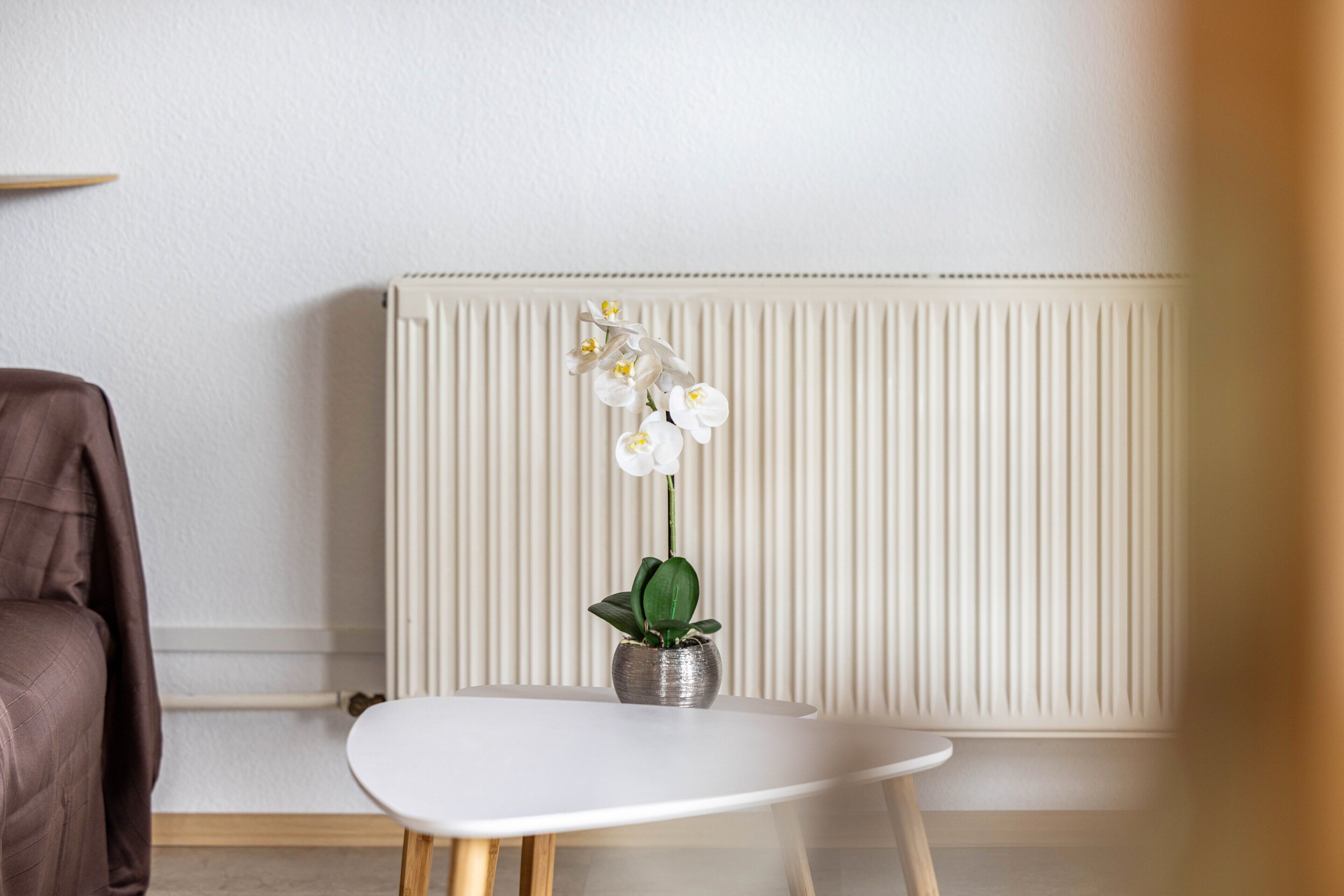 A white radiator, a brown chair, and a white table with a potted orchid.