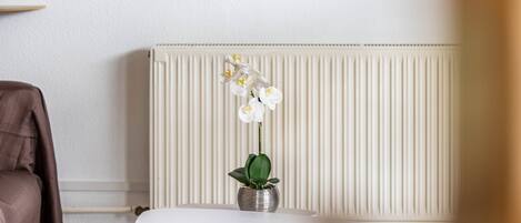A white radiator, a brown chair, and a white table with a potted orchid.