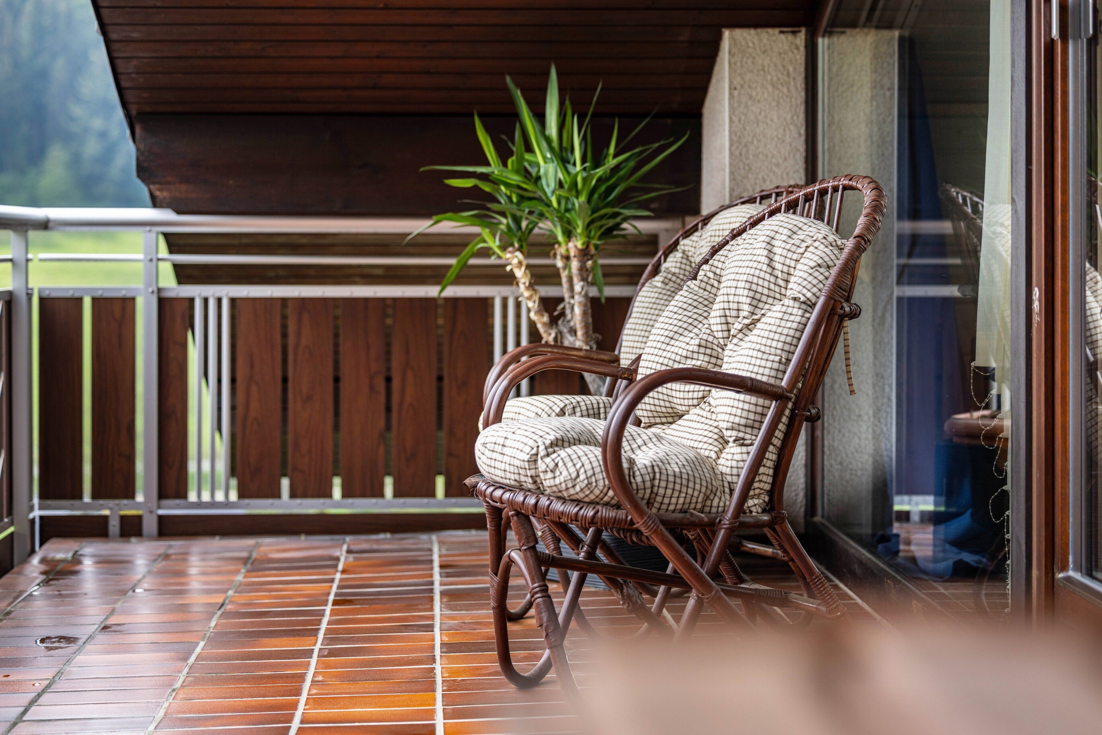 Een rieten stoel met een geruit kussen op een betegeld balkon.