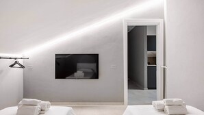Una camera d'albergo moderna con un letto grande, un letto più piccolo, una televisione a schermo piatto montata a parete e una porta che dà su un corridoio.