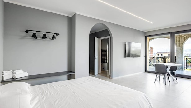 Una moderna camera d'albergo con un letto grande, un angolo salotto con tavolo e sedie, una TV a parete e un balcone con vista.