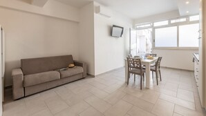 Un salon moderne comprenant un canapé, une table à manger, des chaises et un téléviseur fixé au mur.