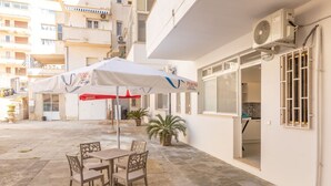 Un espace extérieur aménagé avec une table et des chaises, un parasol et un bâtiment doté d’une fenêtre et d’un appareil de climatisation.