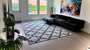 Un salon avec un canapé, un tapis à motifs, un tableau et une vue sur l’extérieur.