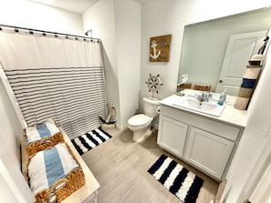 Un baño con cortina de ducha a rayas, un inodoro, un lavabo con espejo y un adorno en la pared.