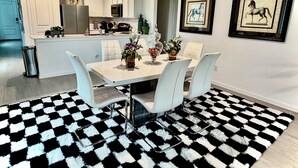 Une cuisine moderne avec des meubles blancs, un réfrigérateur et un four à micro-ondes. On y trouve également un coin repas avec une table, des chaises et un tapis à carreaux noirs et blancs.