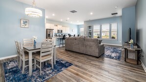 A modern living room with a dining area, kitchen, and large windows. - Coastal Retreat • 3 Kings • Bethany Beach 5 Miles (Millville)