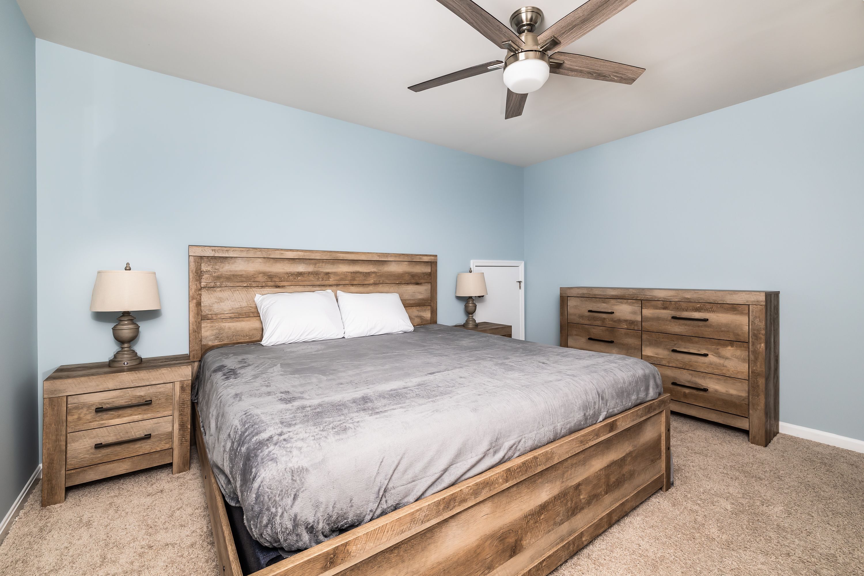 Une chambre à coucher avec un lit en bois, deux tables de chevet, un ventilateur de plafond et un sol recouvert de moquette.