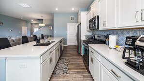 A modern kitchen with white cabinets, a central island, a microwave, and a coffee maker. - Coastal Retreat • 3 Kings • Bethany Beach 5 Miles (Millville)