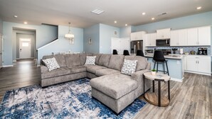 A living room with a sectional sofa, a round coffee table, and a kitchen with white cabinets and stainless steel appliances. - Coastal Retreat • 3 Kings • Bethany Beach 5 Miles (Millville)