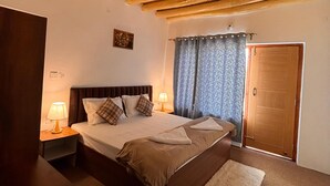 A bedroom with a wooden ceiling, a bed with pillows, a nightstand with a lamp, and a door. - julley ladakh homestay (Leh)