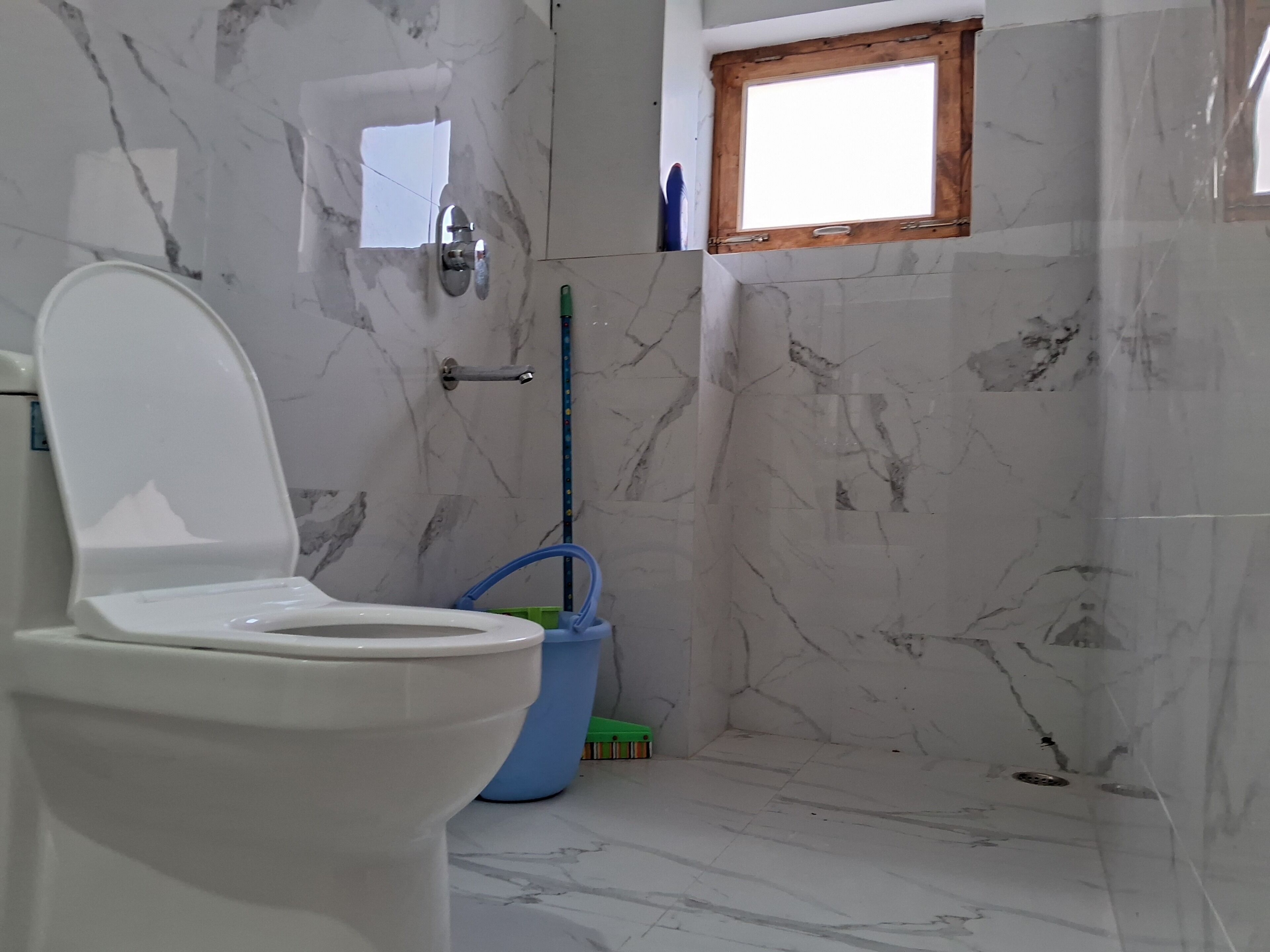 A bathroom with a toilet, a window, a mop, and a shower area.