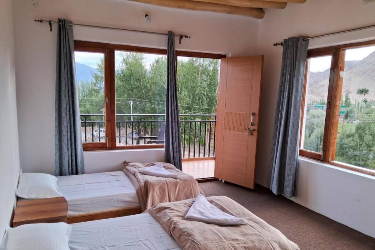 Une chambre dotée de deux lits, d’un balcon et offrant une vue sur la verdure et les montagnes.