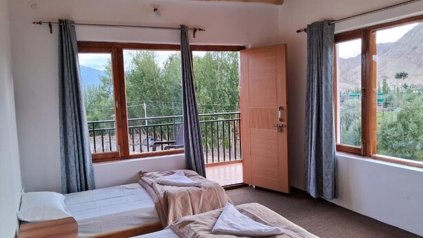 A room with two beds, a balcony, and a view of mountains. - julley ladakh homestay (Leh)