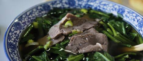 A bowl of soup with beef and greens.