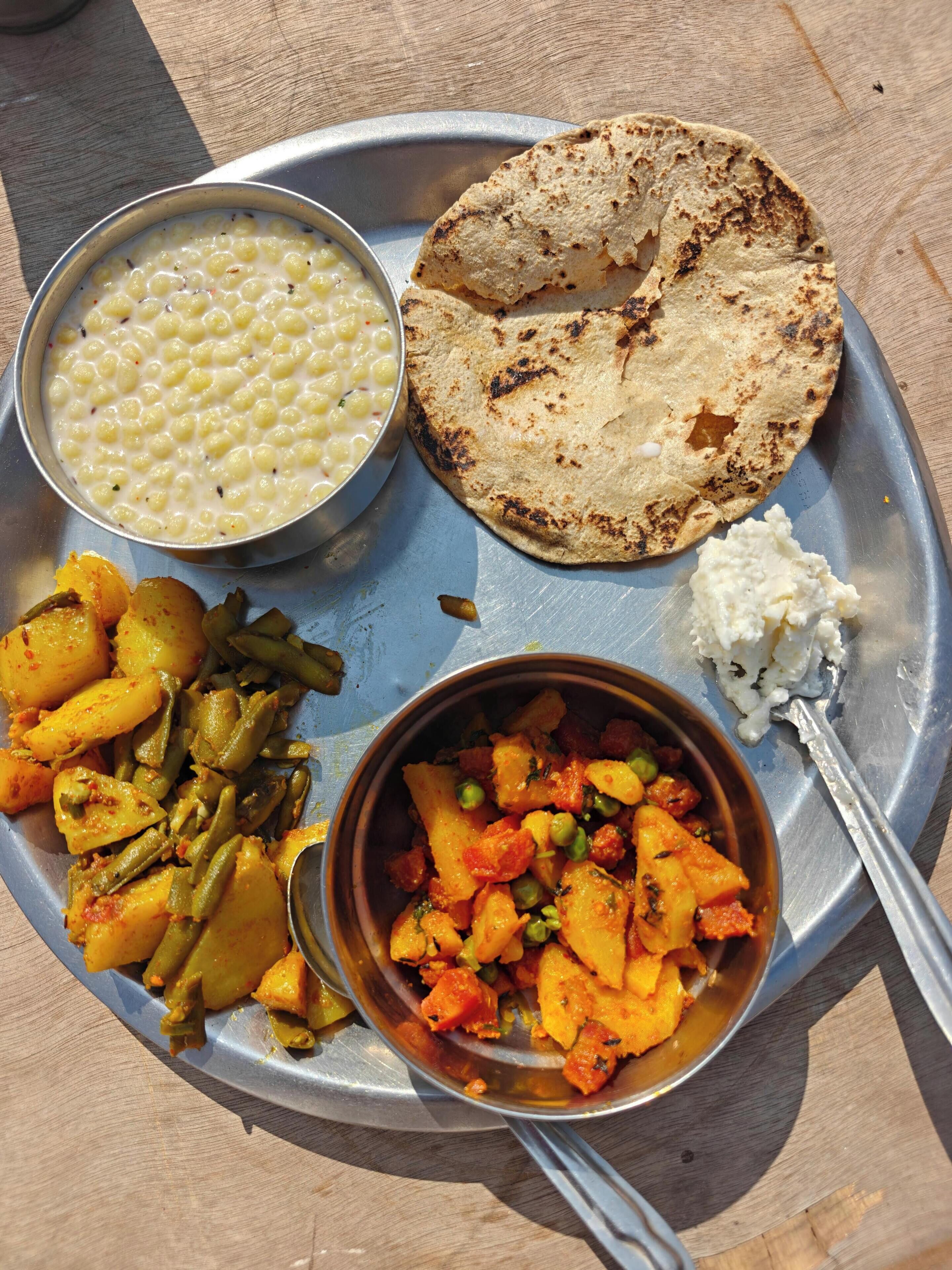 A meal on a metal tray with chapati, dal, mixed vegetables, and a small portion of raita.