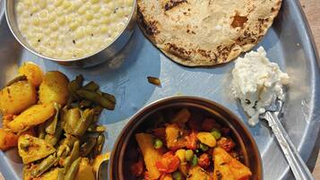 A meal on a metal tray with chapati, dal, mixed vegetables, and a small portion of raita.