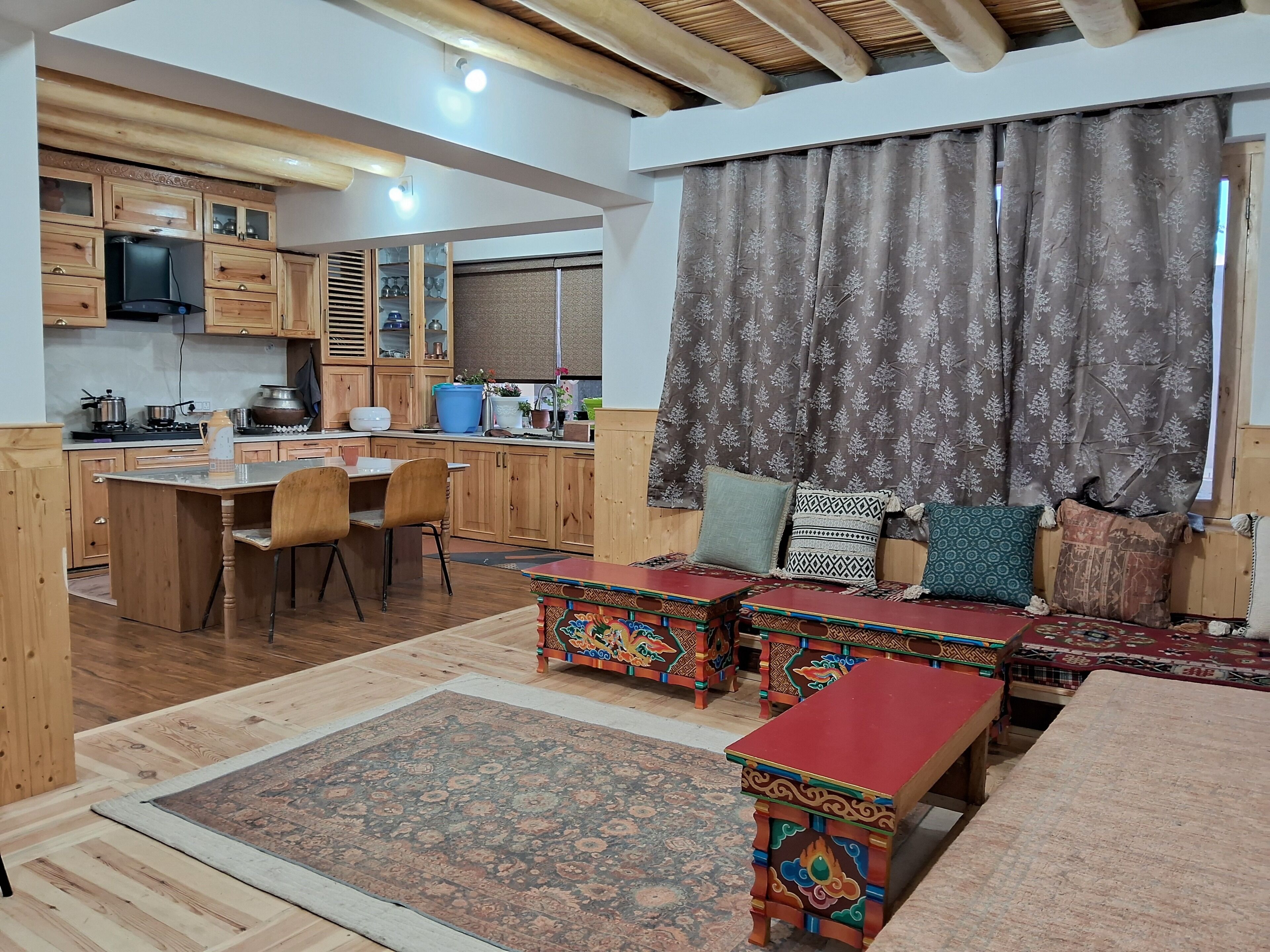 A cozy kitchen with wooden cabinets, a dining area with chairs, a sofa with cushions, and a patterned rug.