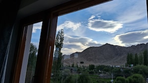 A view through a window with a mountain landscape, including a prominent peak and a valley with greenery and buildings. - julley ladakh homestay (Leh)