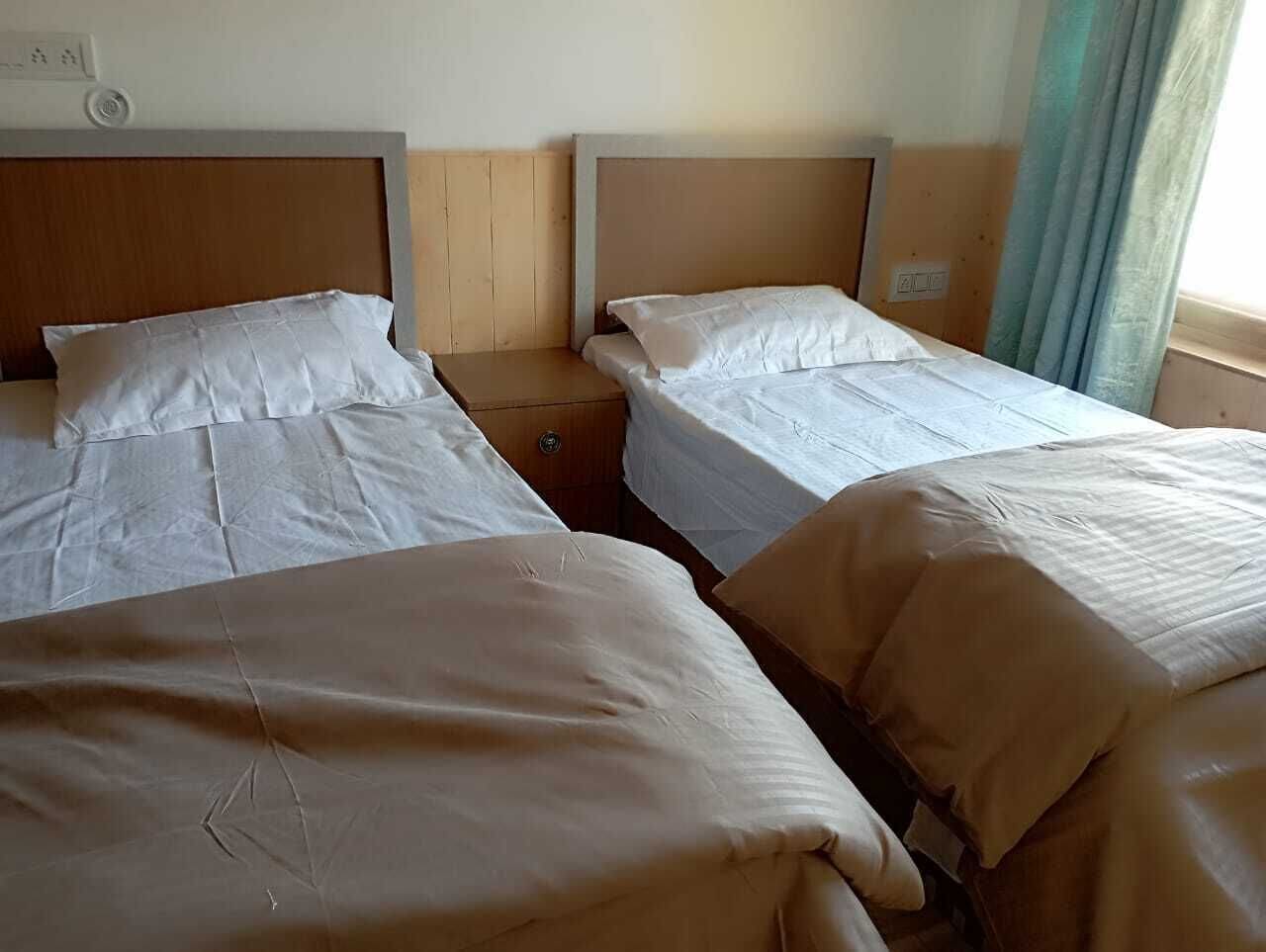 A hotel room with two beds, a wooden headboard, a small bedside table, and a window with curtains.