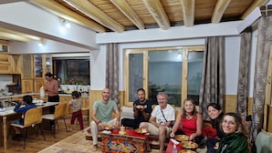 A family dining together in a room with a wooden ceiling and a kitchen in the background. - julley ladakh homestay (Leh)