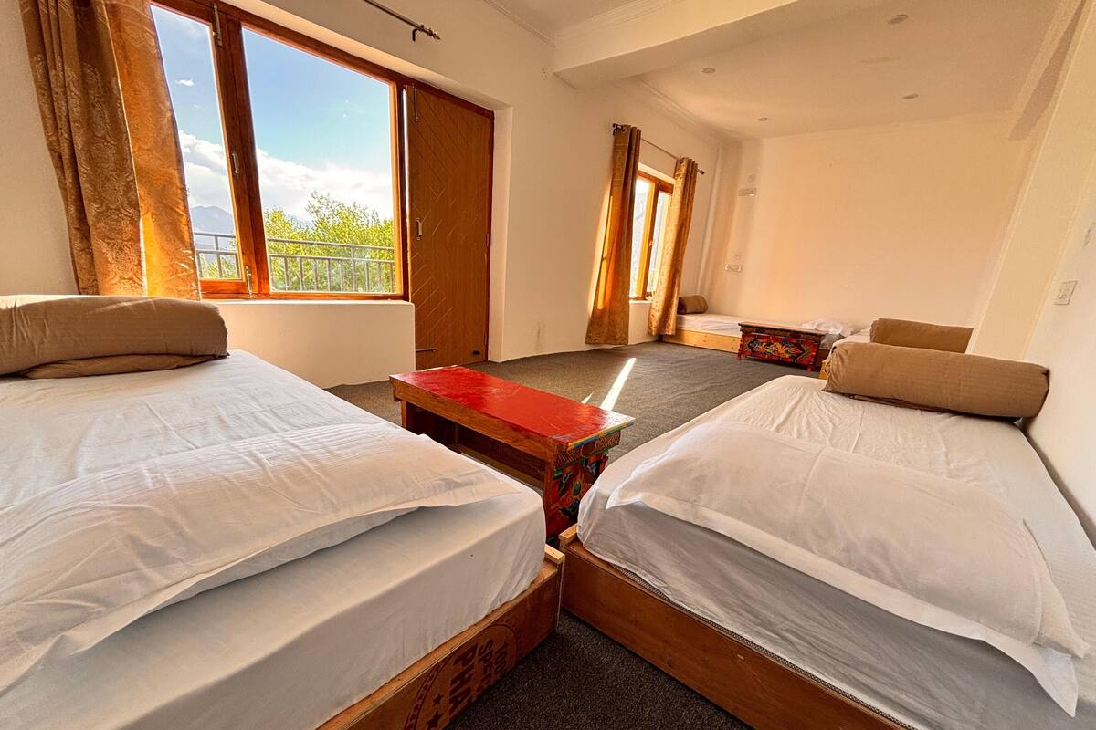 Une chambre avec deux lits, une petite table et une fenêtre avec des rideaux.
