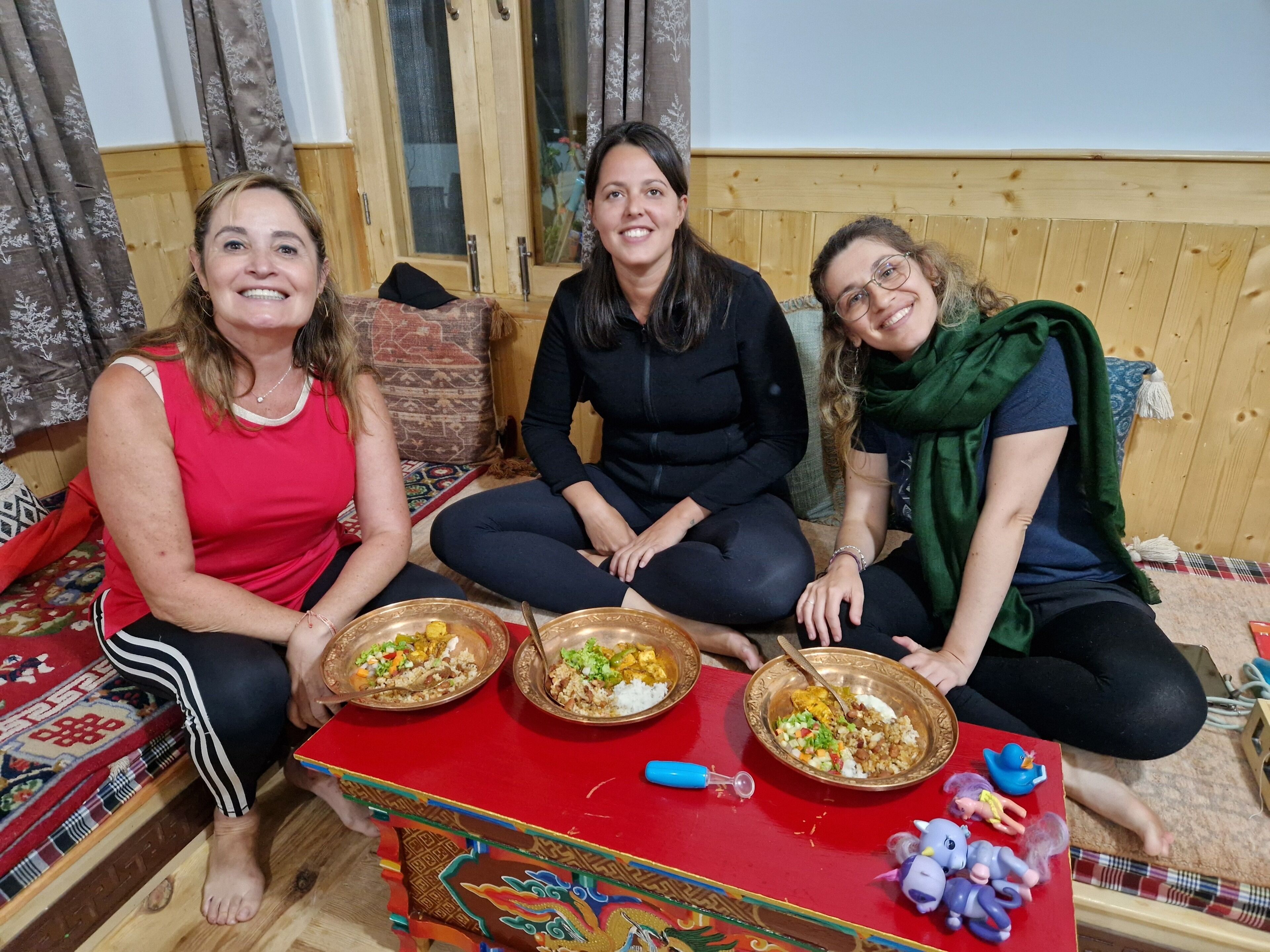 Three people sitting on a couch with a table in front of them holding plates of food.