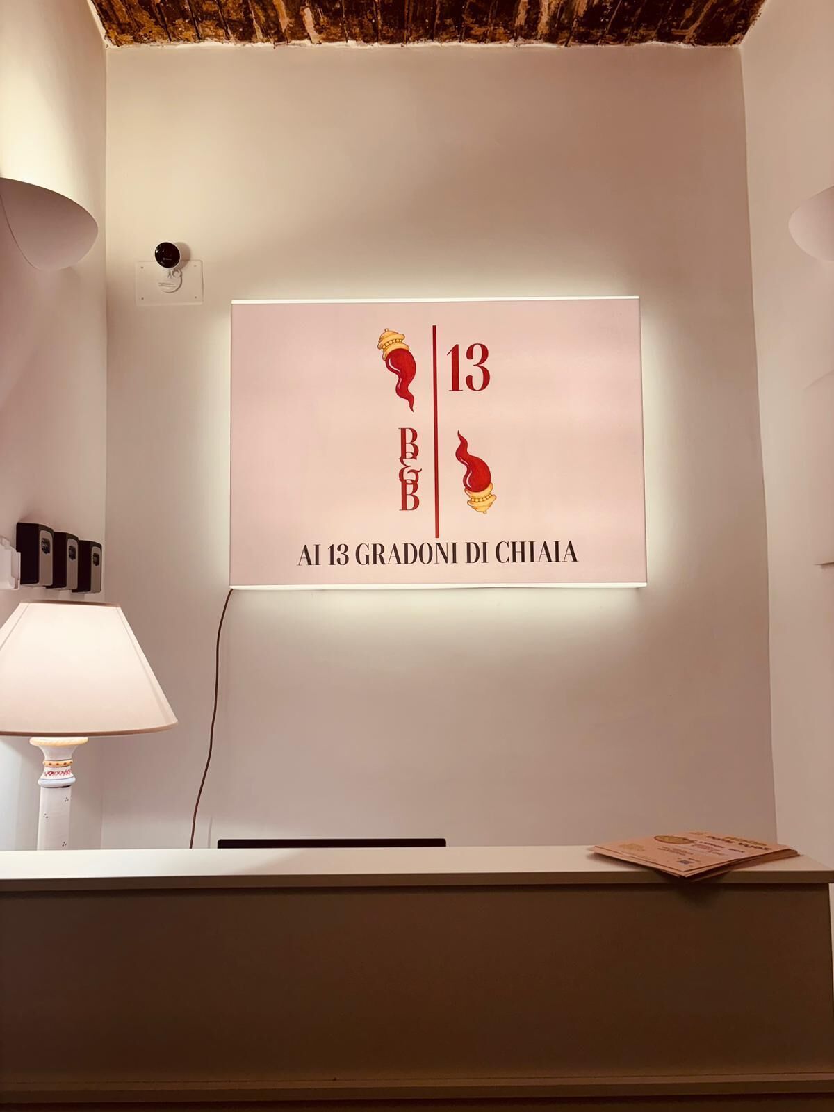A reception desk with a wall-mounted sign displaying '13 BBB' and 'Al 13 Gradi di Chiaia.'