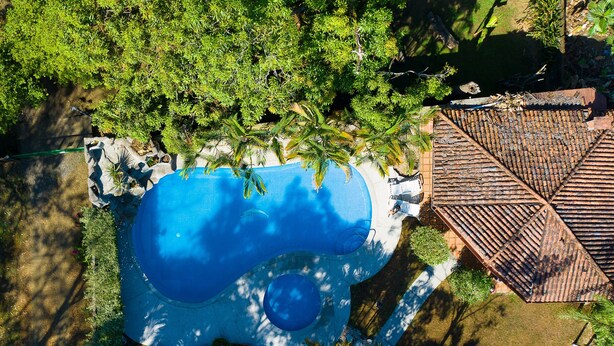 Vista aérea de uma piscina rodeada por vegetação exuberante e uma estrutura de telhado em azulejo.