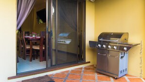 Um pátio com porta de correr, churrasqueira e mesa de jantar com cadeiras.