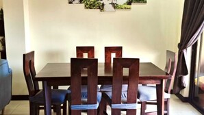 Uma sala de jantar com mesa e cadeiras, um quadro na parede e uma cortina na janela.