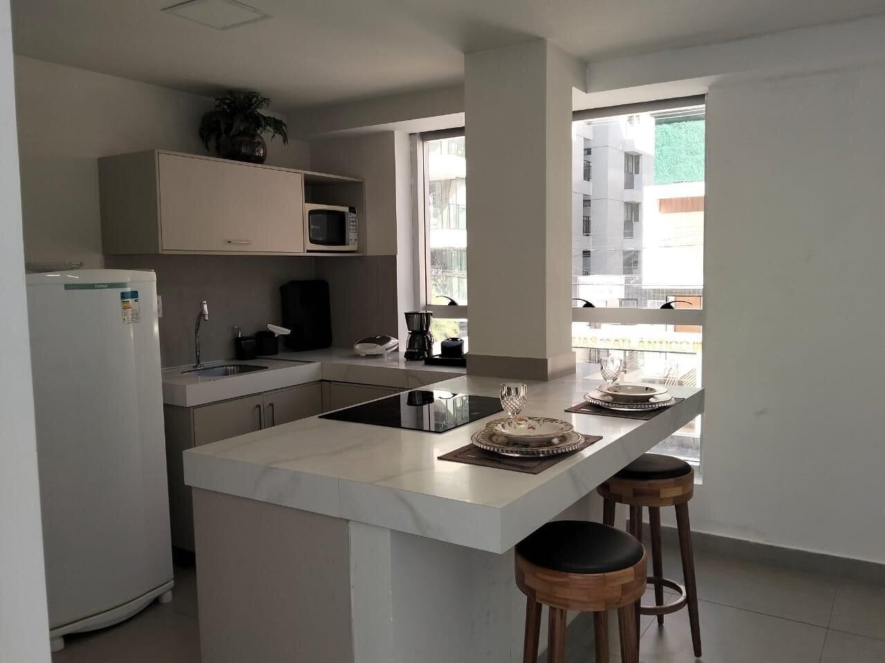 Una cocina moderna con una isla central, taburetes de bar, microondas y refrigerador.