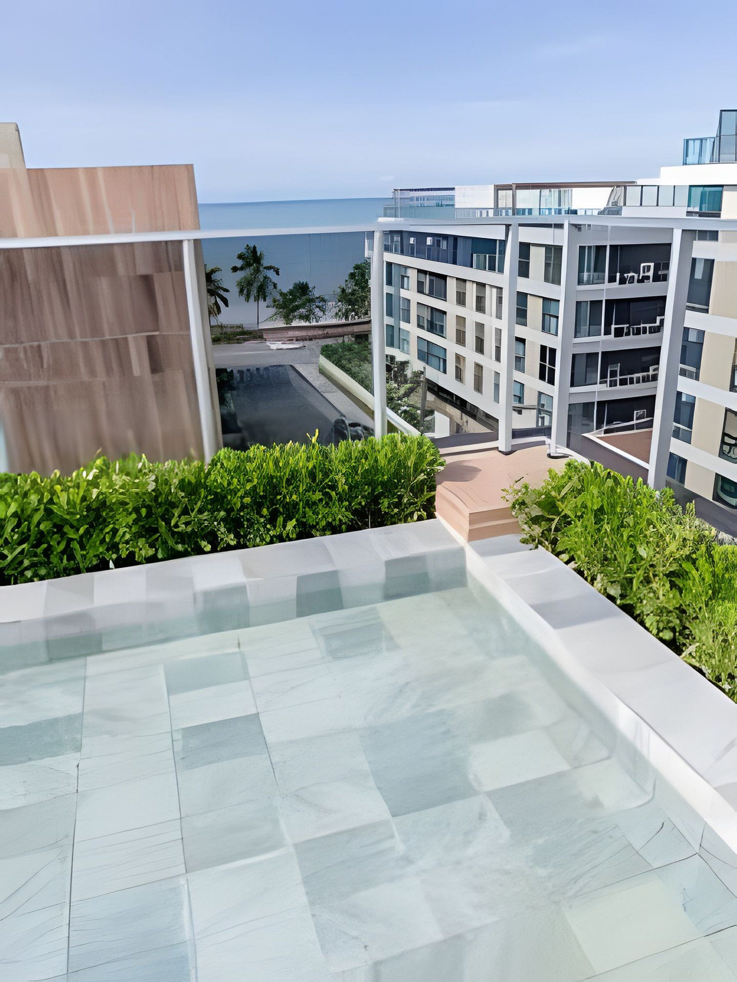 A modern building with a glass facade, a rooftop pool, and a view of the ocean.
