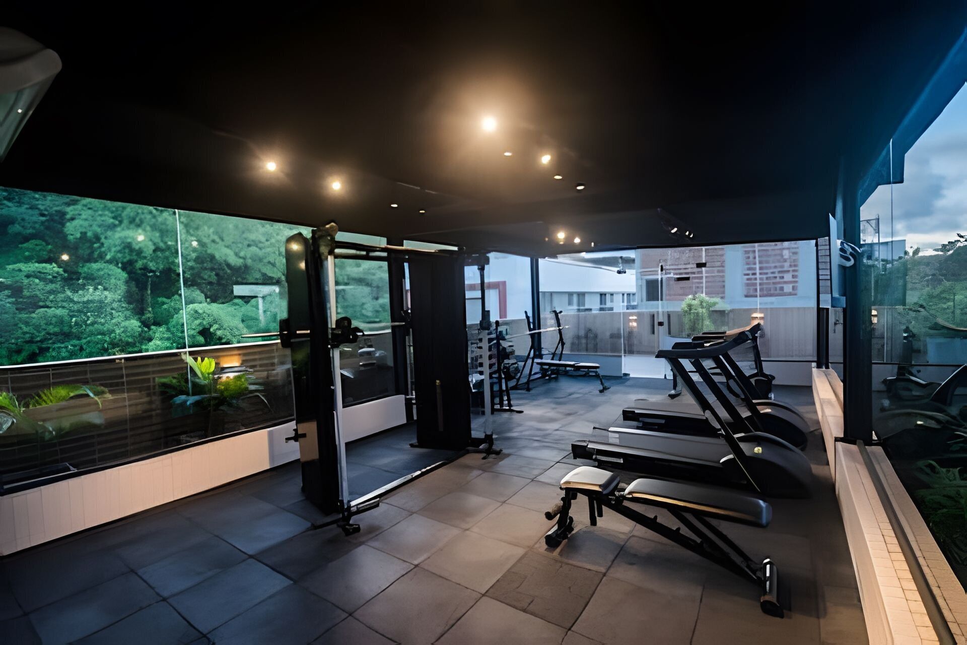 A modern gym with exercise equipment, a large window with a view of greenery, and a glass partition.