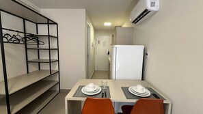 A compact kitchenette with a white refrigerator, a wall-mounted air conditioner, and a dining area with two chairs and a table set for two. - Vivendas do Mar (João Pessoa)